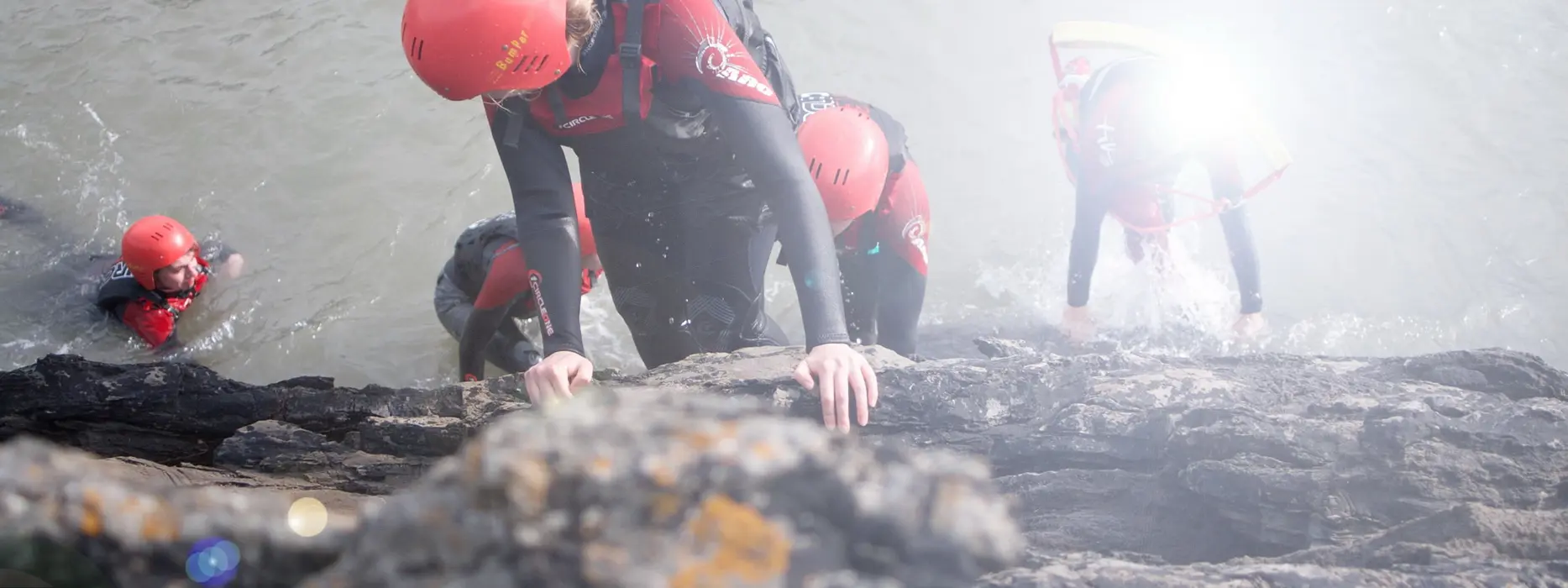 Coasteering participants scrambling across the rocks at Baggy Point near Croyde Bay
